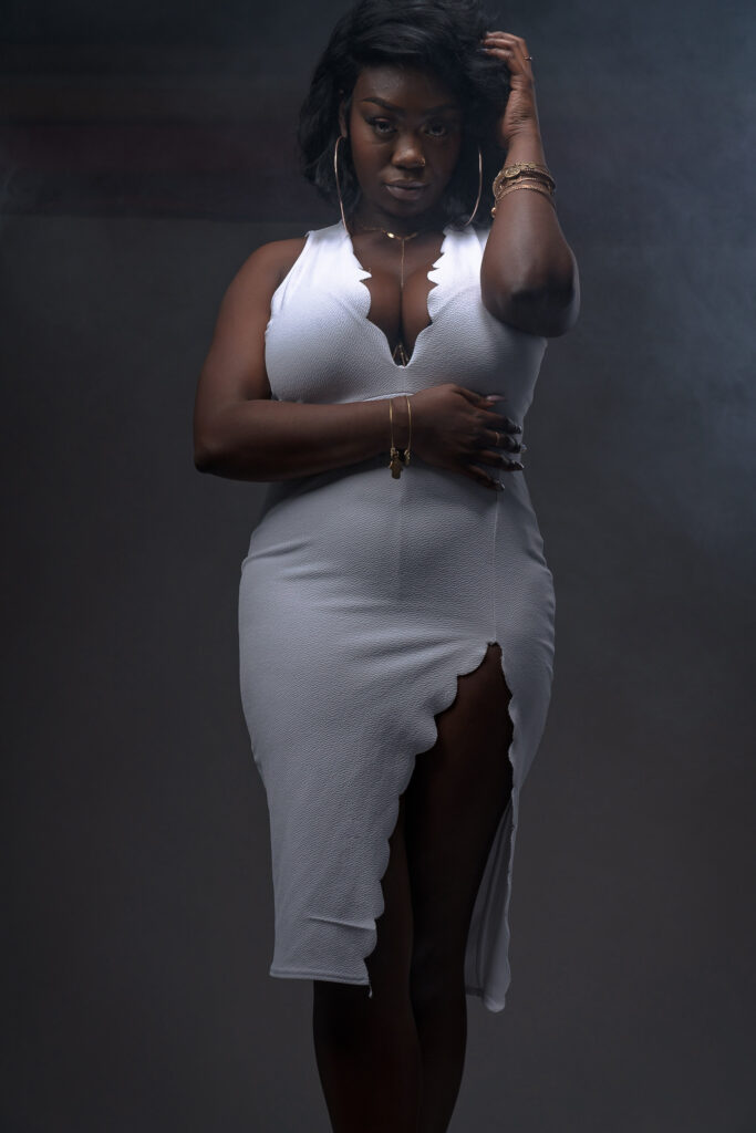 Woman in a fitted gray dress leaning against a dark wall