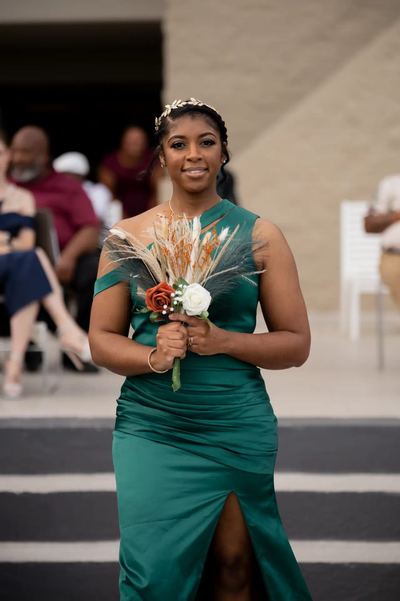 Bridesmaid in emerald green walks down the aisle with a bouquet