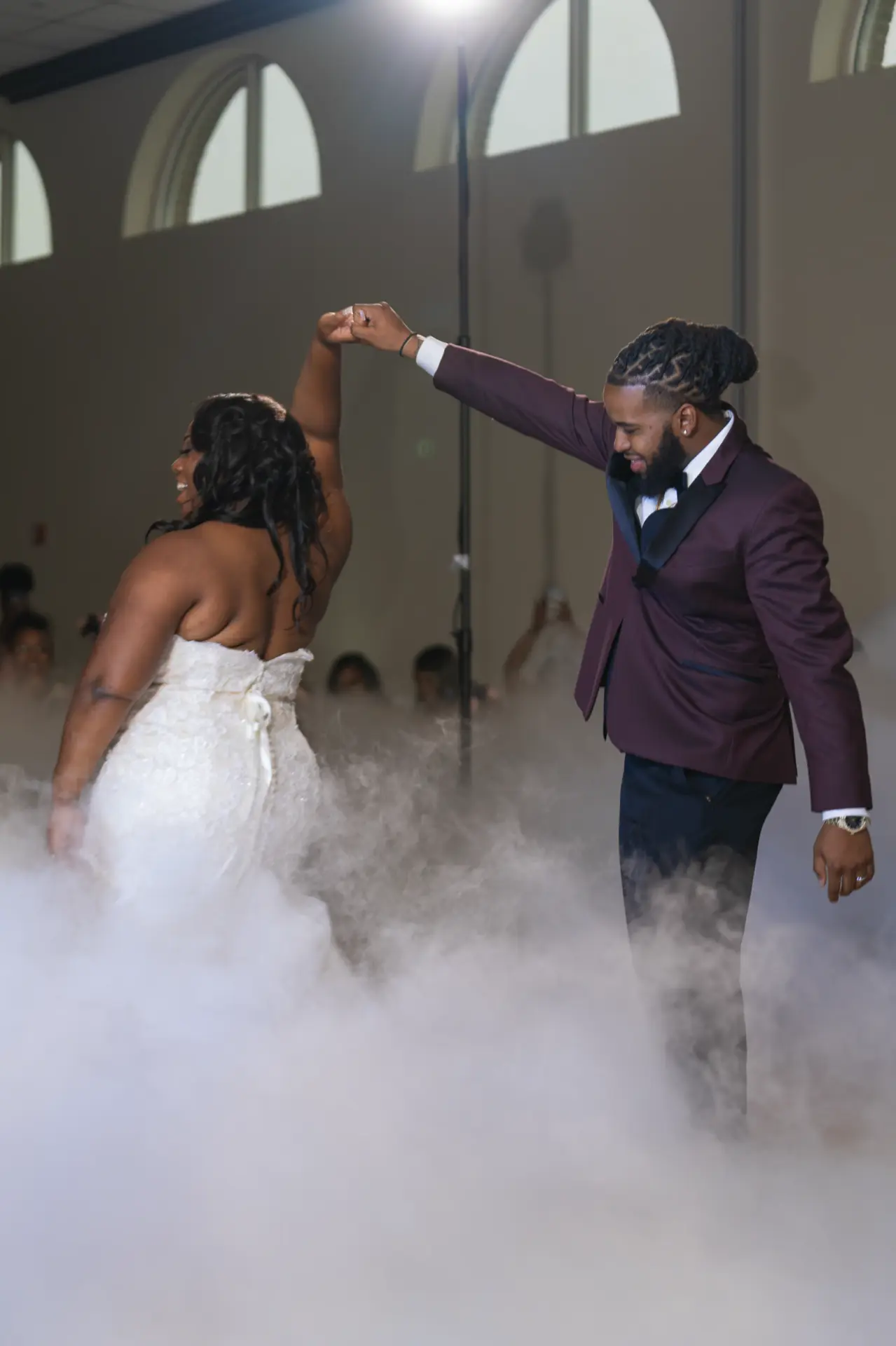 Groom twirling the bride during their first dance through a haze of low fog