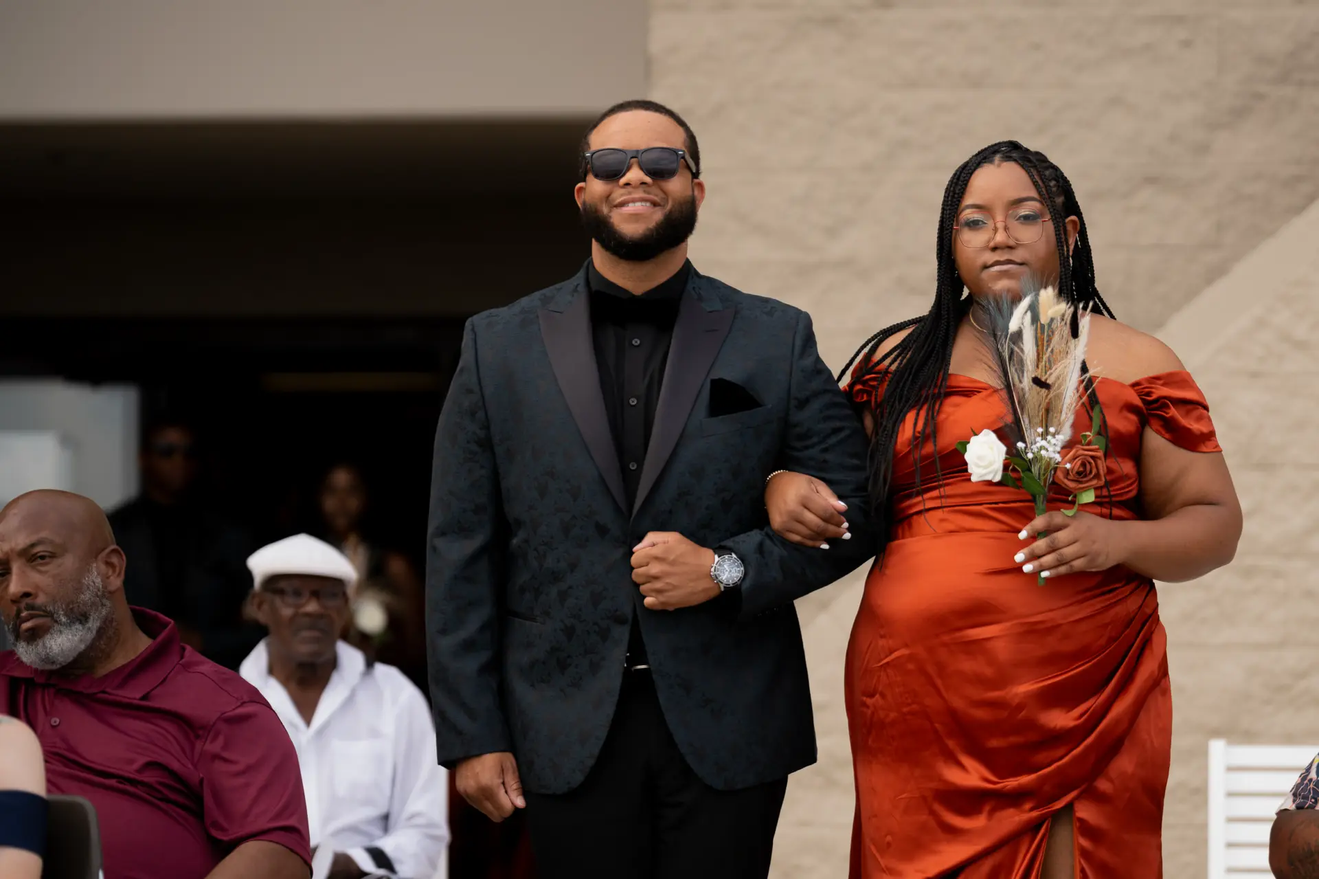 Guest in an orange dress walks arm in arm with a groomsman