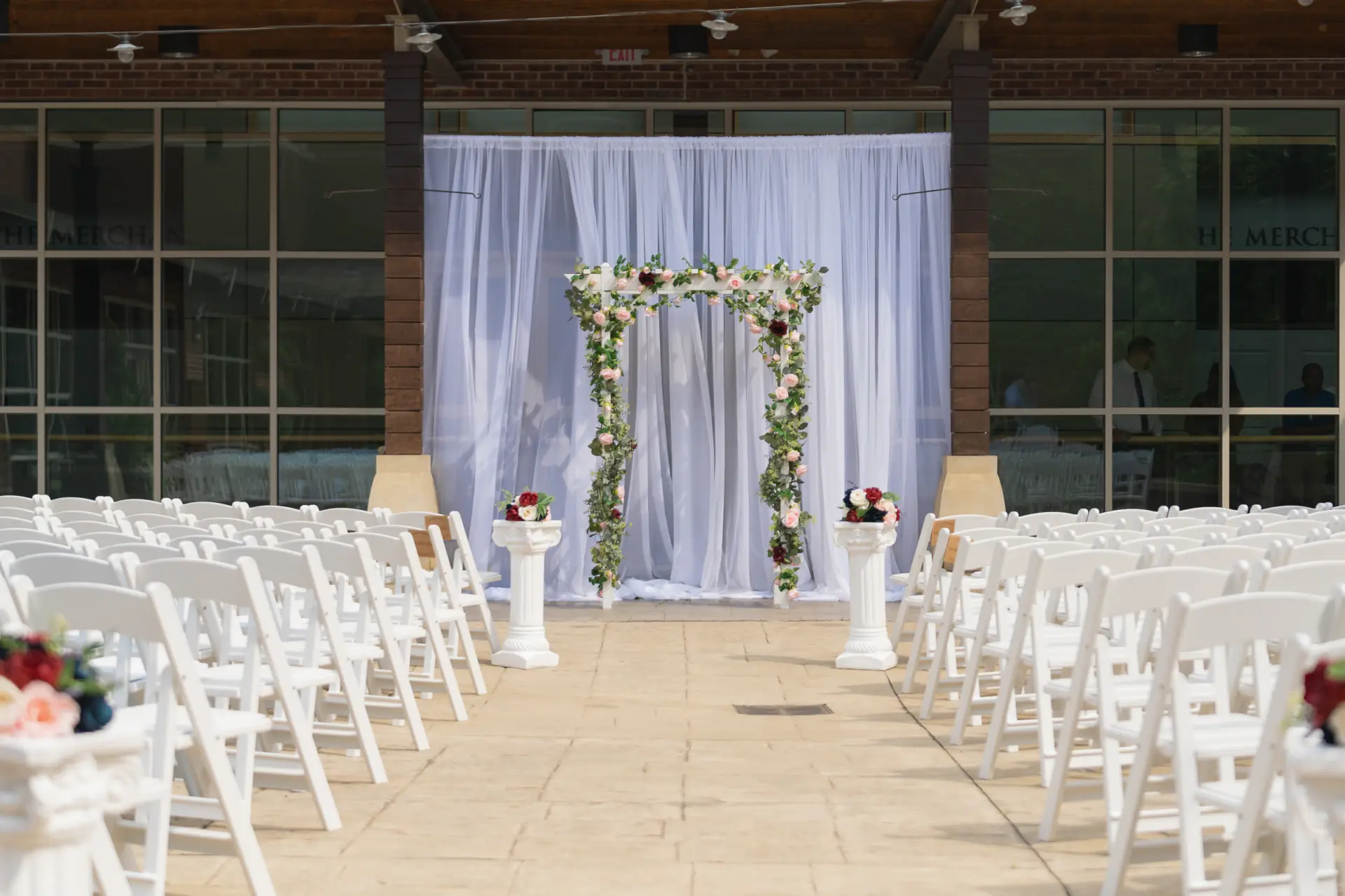 Indoor ceremony room with white chairs, a floral arch and chandeliers