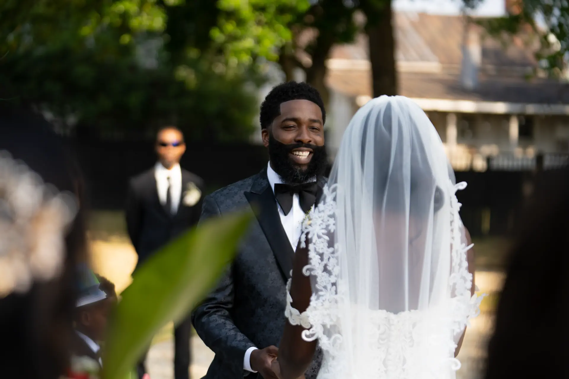 Groom lifts the bride's veil outdoors as guests watch