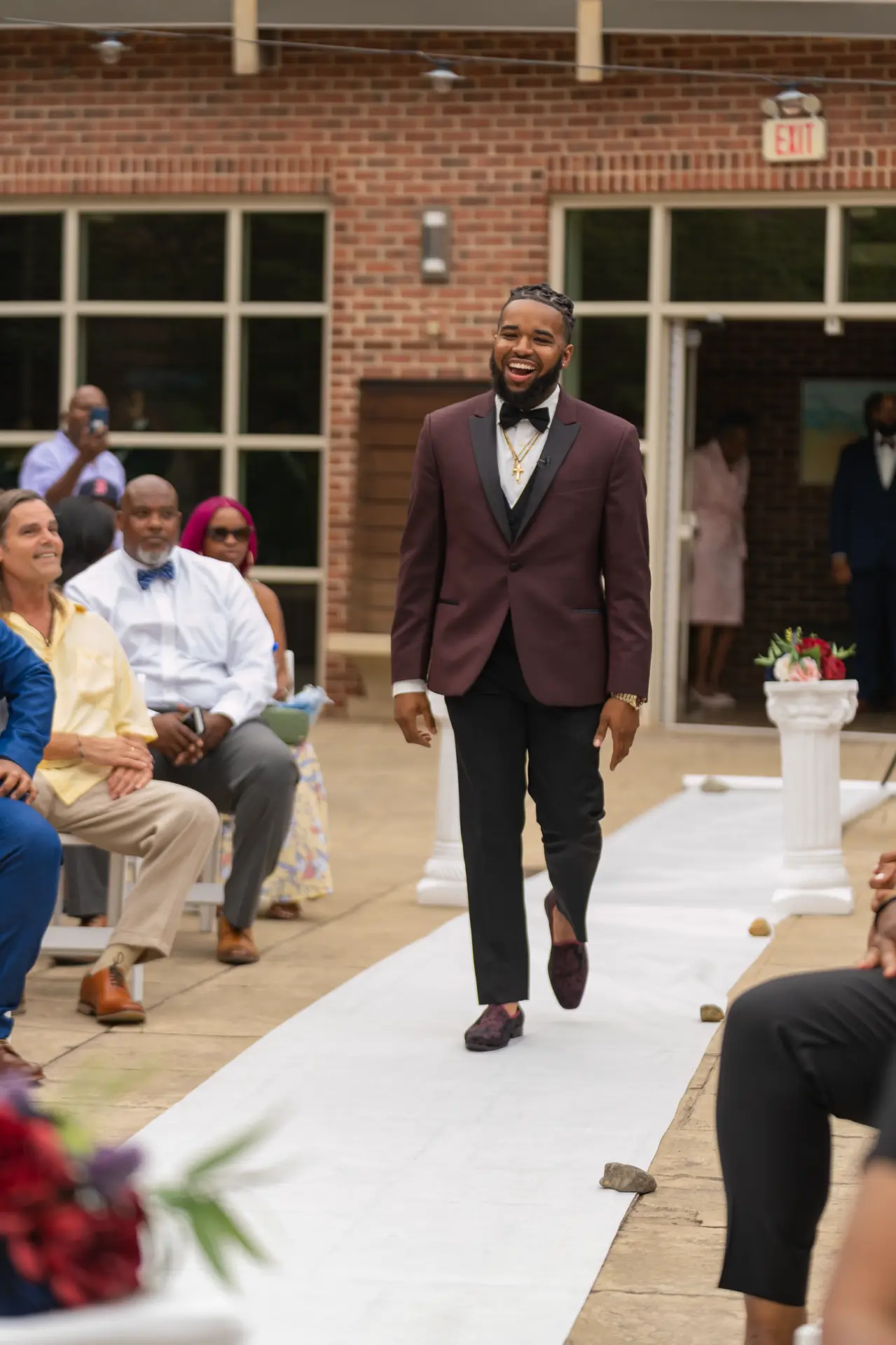 Groom in a tan suit walking down the outdoor aisle between seated guests