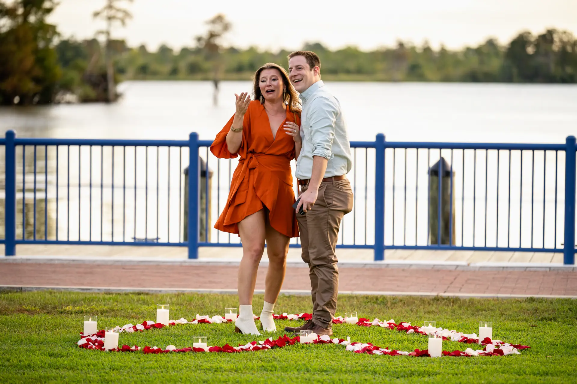 Couple stands on a lakeside lawn with rose petals at their feet